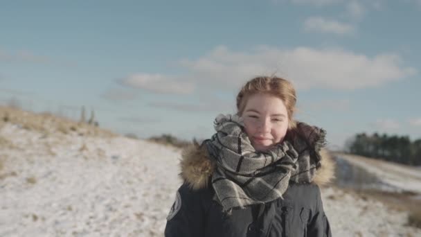 Cámara sigue a lo largo de lado una joven mujer como ella camina en una nieve cubierto tierra — Vídeos de Stock