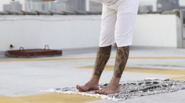 Sakallı adam ayak parmaklarına dokunarak egzersiz yapar sonra da vücudunu tahta bir poza çevirir.
