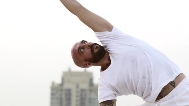 Um cara de Yoga em algodão T-shirt estica seus braços sobre sua cabeça — Vídeo de Stock