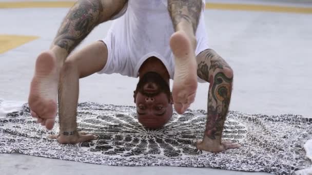 Egy férfi jógázik lábakkal a levegőben és kezekkel a földön. — Stock videók