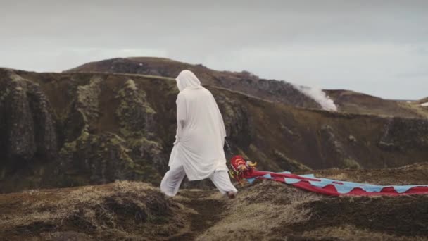 En mann som går på toppen av fjellet, sleper en bit av det tynne stoffet til tau. – stockvideo