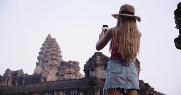 ロングブロンドの髪を持つ若い旅行者は、カメラ電話で壮大な景色を撮ります — ストック動画