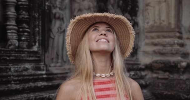 Schöne Frau sieht verblüfft aus vor dem Hintergrund einer antiken Mauer mit aufwändigen Gravuren — Stockvideo
