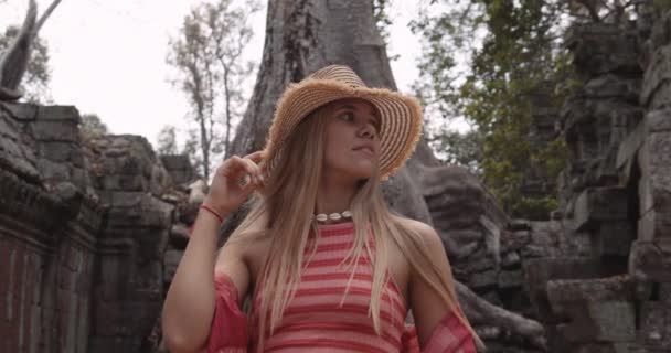 Una modelo rubia sonríe con el telón de fondo de un árbol enorme — Vídeo de stock