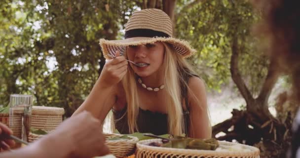 Blondes weibliches Model isst, während sie von grünen Bäumen unter der Sonne umgeben ist — Stockvideo