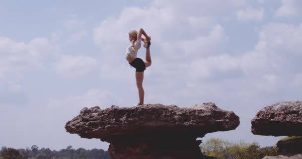 Junge, fitte Frau streckt sich mit einem Bein auf einem riesigen Felsbrocken in der Landschaft — Stockvideo