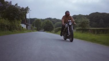 Motosiklet Gri Beton zeminde koşuyor, yemyeşil tarlaları ve ağaçlarıyla.