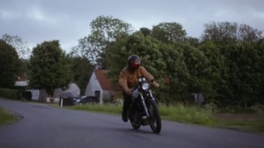 Pürüzsüz bir yolda, yemyeşil bir arazinin arka planında sürülen bir motosiklet.