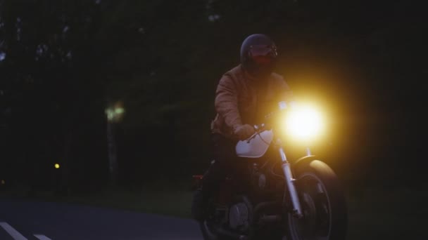 Um tiro de rastreamento completo de uma motocicleta com faróis irradiando em uma estrada escura — Vídeo de Stock