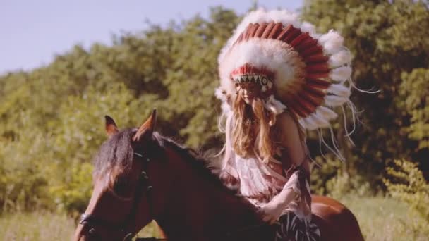 Meisje in indiaanse hoofdtooi te paard in Sunny Meadow — Stockvideo