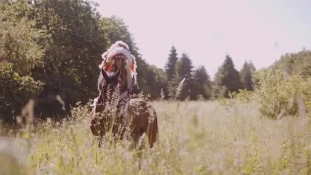 Dziewczyna w indiańskim nakryciu głowy na koniu na łące — Wideo stockowe