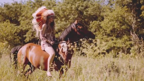 Fiatal nő fejdísszel lovagol a réten. — Stock videók