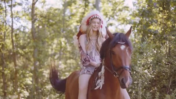 Mosolygó nő fejdísszel ül a lovon a napsütötte erdőben — Stock videók