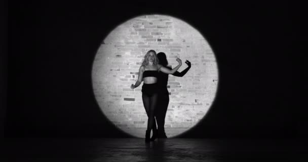 Молода спокуслива жінка в прожекторі танцює на тлі цегляної стіни — стокове відео