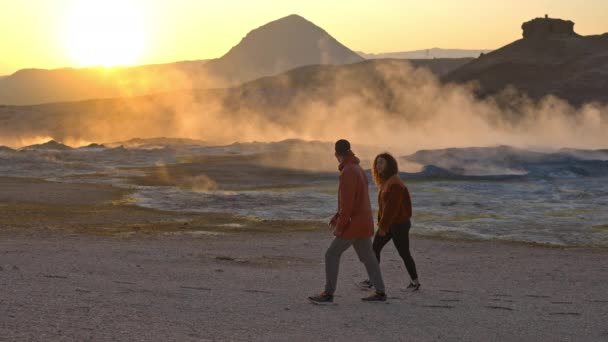 Путешественники, гуляющие по геотермальному полю на фоне горных хребтов — стоковое видео