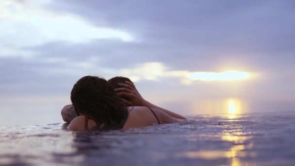 Pareja siendo íntima al borde de la piscina infinita con la vista de la puesta del sol — Vídeo de stock