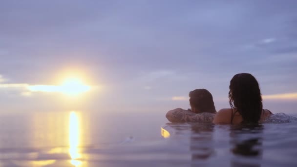 Festői kilátás a pár pihentető a végtelen medencében Élvezi naplemente óceán felett — Stock videók