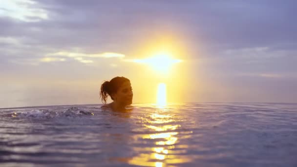Gyönyörű nő mártott egy végtelen medence az arany naplemente alkonyatkor — Stock videók