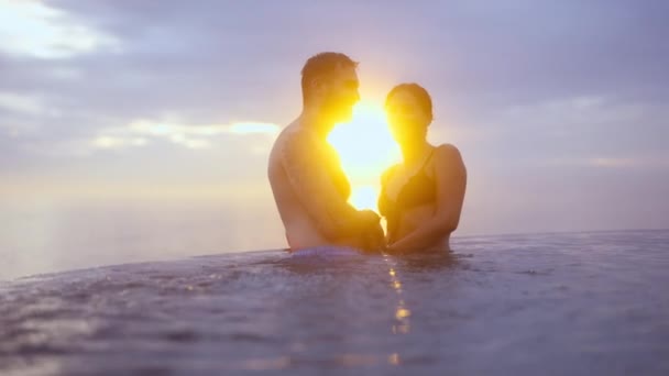 Casal intimamente perto de uma piscina infinita no pôr-do-sol dourado — Vídeo de Stock