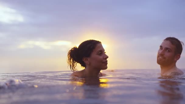 Пара расслабленных на краю бесконечного бассейна с видом на золотой закат — стоковое видео