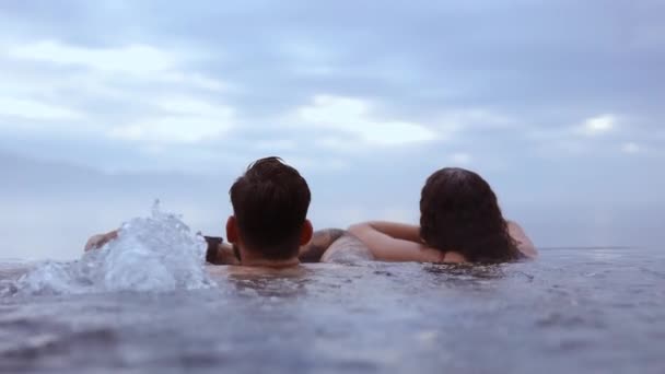 Casal Relaxando em uma piscina infinita com a vista do majestoso céu azul — Vídeo de Stock