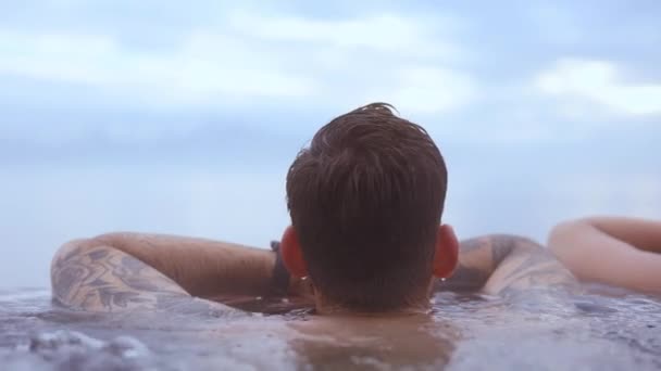 Привабливий вид на людину з татуюванням у воді з величним виглядом на блакитне небо — стокове відео