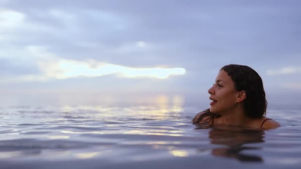 Улыбающаяся модель, погруженная в воду на фоне величественного закатного неба — стоковое видео