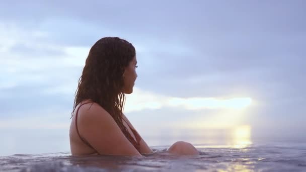 Belle femme assise au bord de la piscine à débordement avec la toile de fond — Video