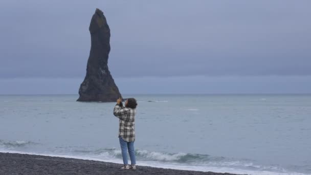 Vista de una viajera apreciando el paisaje en la playa de arena negra — Vídeos de Stock