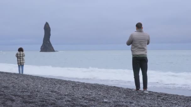 Majestuosa vista de los turistas mirando la escena en la playa de arena negra de Reynisfjara — Vídeo de stock