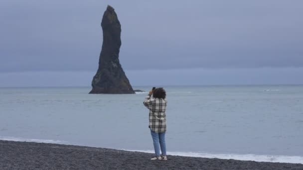 Foto van een toerist aan de kust omringd door Black Sand en Reynisdrangar — Stockvideo