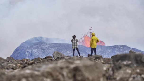 Casal de viajantes apreciando a paisagem de um vulcão em erupção — Vídeo de Stock