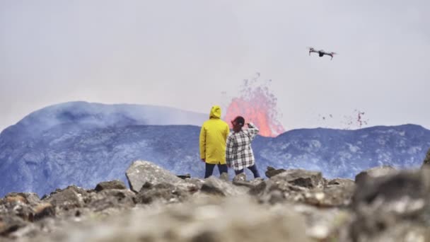 Panoramiczny strzał podróżników spacerujących z widokiem na erupcję wulkanu — Wideo stockowe