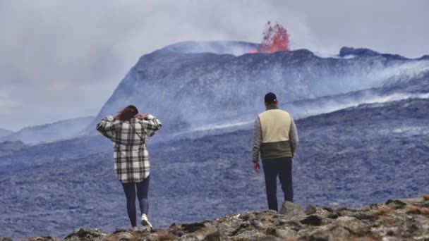 Dva cestovatelé na vrcholu skalnatého pole s výhledem na zničující sopku — Stock video
