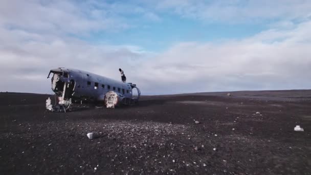 Touristen stehen oben auf dem Flugzeugwrack von Solheimasandur und dem felsigen offenen Feld — Stockvideo