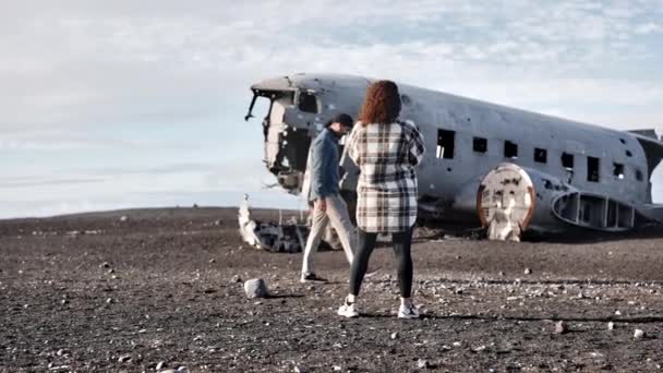 Junge Touristen stehen vor dem Flugzeugwrack von Solheimasandur unter dem Himmel — Stockvideo