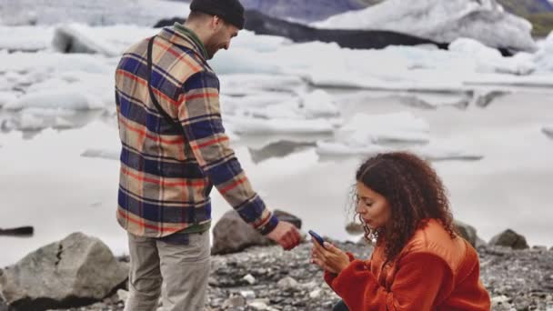 Frau übergibt Handy an lustigen männlichen Touristen - Gletscher im Hintergrund — Stockvideo