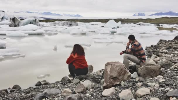 Пара мандрівників, що сидять біля скелі на березі озера і танення льоду — стокове відео