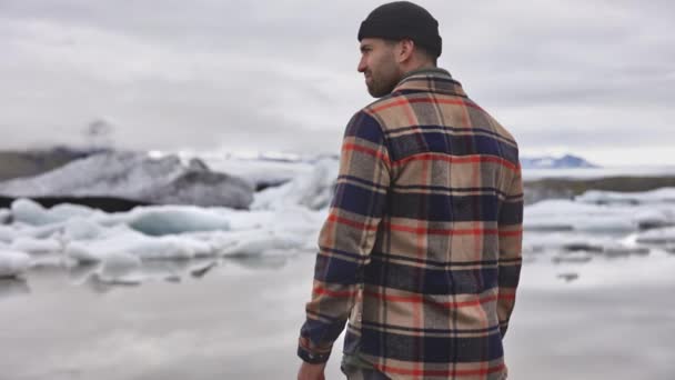 Turista masculino parado entre campos glaciares y lago congelado en Islandia — Vídeos de Stock