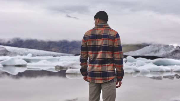 पुरुष यात्री आइसलैंड में ग्लेशियर से भरे जमे हुए झील के दृश्य का आनंद ले रहा है — स्टॉक वीडियो