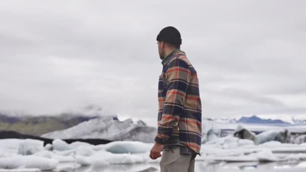 Seitenaufnahme eines Touristen am Ufer des Sees mit schmelzendem Gletscher im Hintergrund — Stockvideo