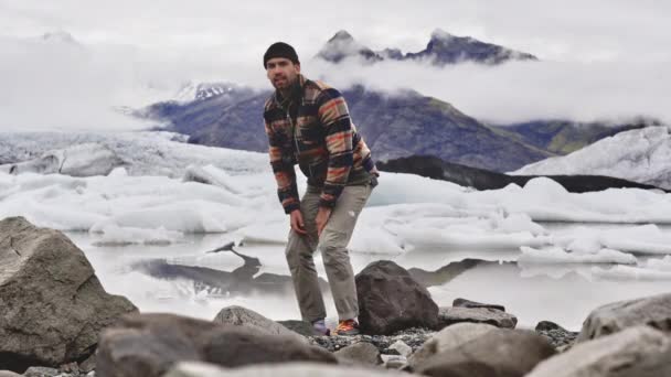 Tourist Getting Up from Rock met uitzicht op ijsberg en berg op de achtergrond — Stockvideo