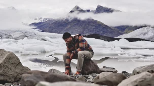 Мужчины бросают камни на таящее замерзшее озеро в Исландии — стоковое видео
