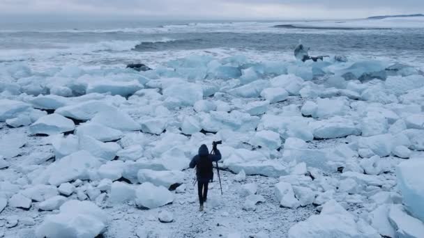 アイスランドの氷河湖の近くのダイヤモンドビーチの写真家の上にドローン — ストック動画