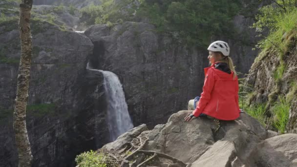 Rock Climber siedzi na skałach naprzeciwko wodospadu — Wideo stockowe