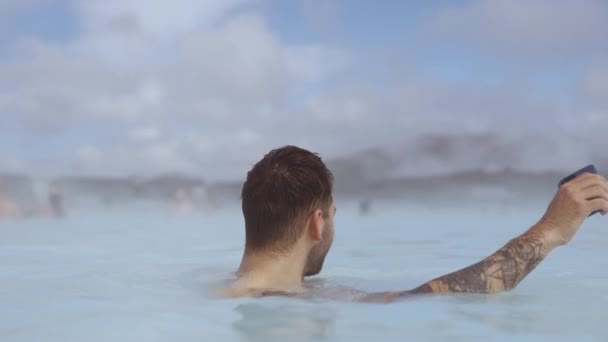 Usmívající se muž s chytrým telefonem v Lagoon geotermální lázně — Stock video