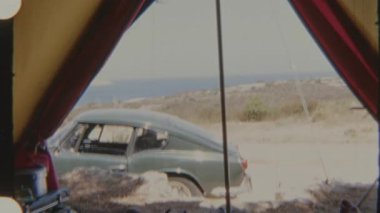 Bu eski 1970 'lerin 8mm' lik film görüntüleri, Korsika 'da tozlu bir kıyı manzarasında klasik bir arabaya bakan renkli bir çadırın içini gösteren nostaljik bir kamp sahnesi çeker.