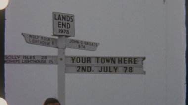 1978 'de bir kadın Lands End tabelasının önünde duruyor, 8 mm' lik bir filmde çekilmişti, dayanıklı, kayalık bir zemine karşı..