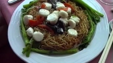 Deniz tarağı, mantar ve kırmızı biberle kaplı bir tabak çıtır altın erişte zarif bir Kore yemek ortamında taze yeşil sebzelerle çevrilidir.