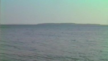 Minimalist bir kıyı manzarası, ufukta beliren sisli gökyüzü ile kumlu bir sahil boyunca yumuşak su hareketlerini yakalar.